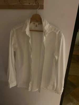 Vit klassisk skjorta med krage - En stilren vit skjorta med klassisk krage och långa ärmar. Skjortan är rak i modellen och har knappar framtill. Perfekt för en clean och enkel look. Tillverkad i bomull för en skön känsla.