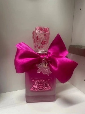 Juicy Couture Viva La Juicy Petals Please - Juicy Couture Viva La Juicy Petals Please är en parfym i en rosa glasflaska med dekorativt lock med blommönster och en stor, glansig rosa rosett. Flaskan har en charmig blomma som hänge och rymmer 50 ml Eau de Parfum. Perfekt för dig som älskar söta och blommiga dofter. Flaskan är som ny, bara litet tagit ur den.