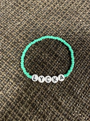 Turkost pärlarmband med text - Snyggt armband med små turkosa pärlor och vita bokstavspärlor som stavar 'LYCKA'. Perfekt accessoar för dig som vill ha något personligt och färgglatt på handleden. Elastiskt band som gör det enkelt att ta på och av.