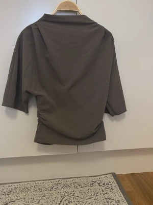 Brun topp med vida ärmar från Gina Tricot - Snygg brun topp från Gina Tricot i storlek XS. Modellen har vida, korta ärmar och en lösare passform men går in vid midjan med lätt drapering på sidorna. Använd ett fåtal gånger 