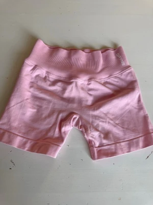 Rosa träningstights-shorts från DFYNE - Säljer ett par ljusrosa träningstights-shorts från DFYNE med hög midja och ribbad linning. Shortsen är tillverkade i ett stretchigt material som passar perfekt för träning. De har en scrunch-detalj bak för extra form och komfort. De är helt nya med prislapp!