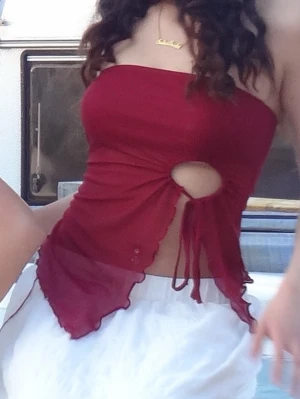 Vinröd tubtopp med snörning - Trendig vinröd tubtopp med snygg cut-out och snörning framtill. Toppen har vågiga kanter och är croppad, perfekt för en cool och ungdomlig stil. Materialet känns lätt och luftigt.