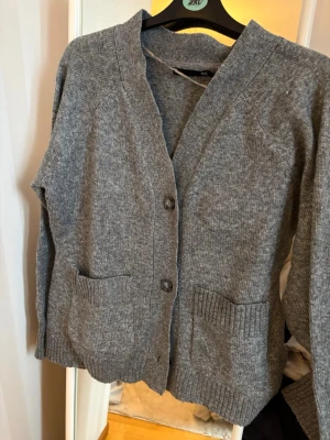 Grå kofta från 157 med fickor - Mysig grå kofta från lager 157 med knäppning framtill och två stora fickor. Koftan har en rak passform, ribbade muddar och v-ringad hals. Perfekt att slänga på sig över en t-shirt. 🩶