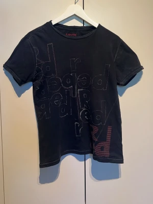 Svart t-shirt från Levi's med tryck - Cool svart t-shirt från Levi's med grafiskt tryck i olika färger och stilar på framsidan. Klassisk rund hals och korta ärmar. Tillverkad i mjuk bomull som känns skön mot huden. Perfekt för dig som gillar streetwear och vill ha något unikt i garderoben.