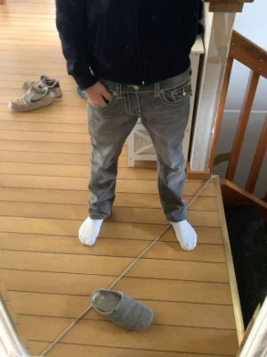 Grå baggy jeans med vita sömmar - Säljer ett par gråa baggy jeans med tydliga vita kontrastsömmar och detaljerade fickor. Jeansen har låg midja och avslappnad passform, perfekta för en chill streetwear-look. Passar dig som gillar en lite lösare stil.