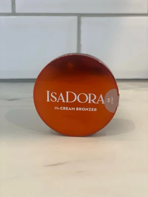 Isadora The Cream Bronzer 46 Light - Krämig bronzer från Isadora i nyansen 46 Light. Kommer i en rund, kompakt burk med brun och orange tonad förpackning. Perfekt för att skapa en naturlig solkysst look med enkel applicering.