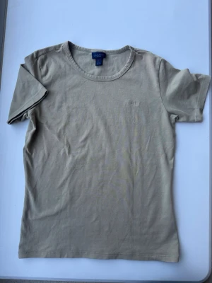 Beige t-shirt från GANT i bomull - Snygg beige t-shirt från GANT med diskret broderad logga på bröstet. Klassisk rund halsringning och korta ärmar. Tillverkad i mjuk bomull som känns skön mot huden. Perfekt basplagg till garderoben.