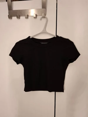 Svart croppad t-shirt - En enkel och stilren svart croppad t-shirt från Shein. T-shirten har rund halsringning, åtsittande passfrorm och korta ärmar.