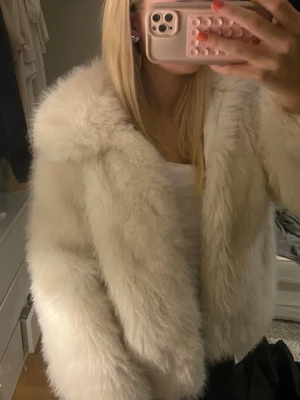 Vit fluffig pälsjacka - Säljer en supermjuk och fluffig vit pälsjacka med bred krage. Jackan har en rak passform och är perfekt för att hålla värmen under kalla dagar. Materialet är fuskpäls som ger en lyxig känsla och snygg look.