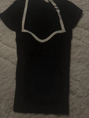 Svart ribbad topp från Gina Tricot - Svart ribbad topp från Gina Tricot med kontrasterande vita kanter och korta ärmar. Toppen har en med kantdetaljer som ger en cool och trendig look. Perfekt att styla med jeans eller kjol.