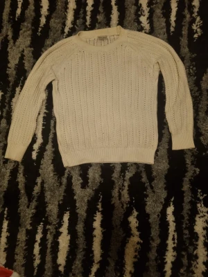 Vit stickad tröja med hålmönster - Snygg vit stickad tröja med hålmönster och rund hals. Tröjan har långa ärmar och ribbade muddar vid ärmslut och nederkant. Perfekt för lager på lager och ger en clean look till din outfit.