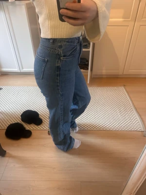 Blå raka jeans med hög midja - Säljer ett par klassiska blå jeans med rak passform och hög midja. Jeansen har fem fickor och stängs med knapp och dragkedja. Perfekta för dig som gillar en avslappnad och tidlös look. Materialet är denim och färgen är ljusblå.