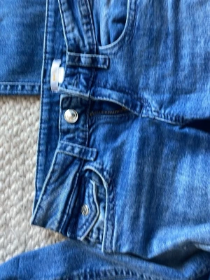Blå jeans med broderad bakficka - BOOTCUT🤍 Säljer ett par klassiska blå jeans i denim med snygg broderad detalj på bakfickan och silverfärgade knappar. Jeansen har normal midja, dragkedja och knappstängning samt fickor både fram och bak. Perfekta för en avslappnad och trendig look.