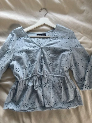 Ljusblå blus  - Säljer en söt ljusblå blus från Pieces med broderade blommor, v-ringning och knytband i midjan, knappt använd!❣️