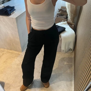 Svarta vida kostymbyxor från madlady  - Snygga svarta kostymbyxor med hög midja och vida ben. Byxorna har pressveck framtill, sidofickor och bälteshällor. Perfekta för en clean och stilren look. Materialet ser ut att vara en mjuk och följsam textil som ger en dressad känsla.