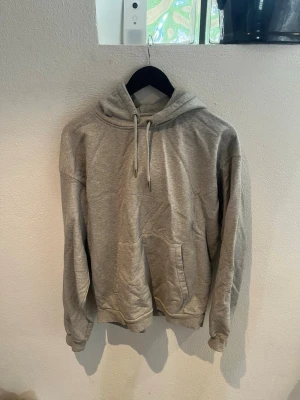 Grå hoodie från A Day's March - Säljer en klassisk grå hoodie från A Day's March i storlek medium. Hoodien har huva med dragsko, stor magficka och ribbade muddar vid ärmar och nederkant. Tillverkad i mjukt bomullsmaterial, perfekt för en avslappnad och stilren look.