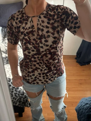  blus från Stockh LM - Säljer en snygg blus från Stockh LM i storlek 36 med leopardmönster i beige, brunt och svart. Blusen har korta ärmar och en liten öppning framtill vid halsen. Perfekt för dig som vill sticka ut med ett coolt mönster.
