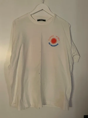 Vit t-shirt med tryck från vero Moda - Vit t-shirt från vero Moda med färgglatt tryck på bröstet där det står 'Le Soleil La Mer Les Vacances' och en röd sol. Klassisk rund hals och korta ärmar. Perfekt för en avslappnad och trendig look.