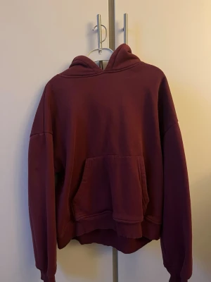 Vinröd hoodie med magficka - Mysig vinröd hoodie med stor huva och rymlig magficka. Oversized passform med långa ärmar och ribbade muddar. Perfekt för en avslappnad och trendig stil. Tillverkad i mjukt bomullsmaterial.