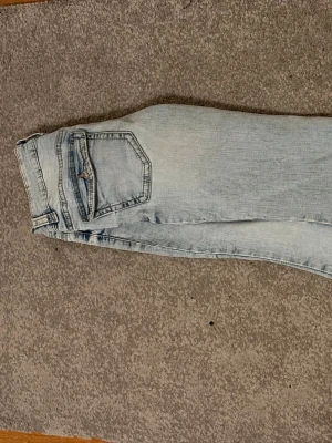 Ljusblå slim fit jeans - Säljer ett par ljusblå slim fit jeans med klassisk femficksdesign och dragkedjegylf. Jeansen har en tvättad look med slitningar och är tillverkade i denim. Perfekta för en avslappnad och trendig stil.