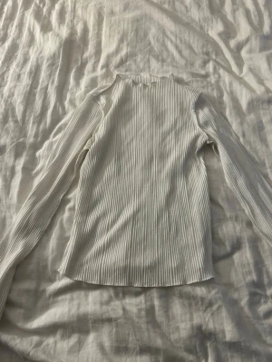 Vit ribbad långärmad topp Bik Bok - Säljer en vit ribbad långärmad topp från Bik Bok i storlek XS. Toppen har en hög hals och är tillverkad i ett stretchigt material som sitter snyggt på kroppen. Perfekt att styla med jeans eller kjol för en clean look.
