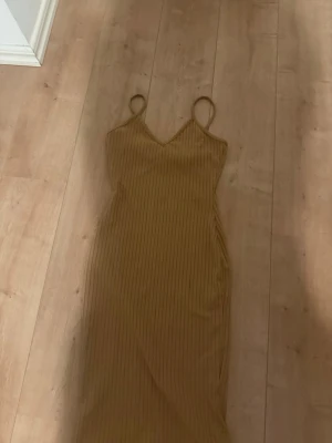 Beige ribbad långklänning - Snygg beige långklänning med smala axelband och v-ringad hals. Klänningen har en ribbad struktur som ger en trendig look och är perfekt för varmare dagar. Passar dig som gillar enkel men stilren design.