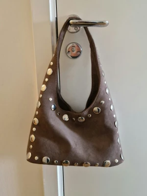 Ljusbrun väska med nitar i fuskmocka - Använd två gånger. Stängs med magnet i mitten. Nypris 379kr.