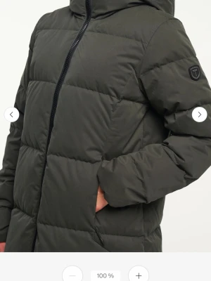 Mörkgrön lång dunjacka med huva - Stella Down Coat är en varm och bekväm vinterjacka med vattenavvisande ytterlager och dunfyllning. Den har huva och dragkedja, perfekt för kalla dagar. Maskintvätt 30 °C  Använd endast två gånger, i nästan nyskick.  Nypris: 2799 kr. Säljes för 1800 kr (kan diskuteras:)