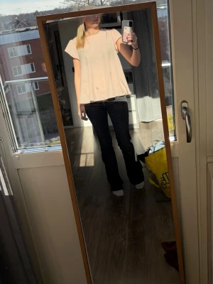 Ljusrosa vid blus med kort ärm - Söt ljusrosa blus med lös passform och korta ärmar. Blusen har en rund halsringning och en snygg detalj med öppning i ryggen. Tillverkad i ett lätt och luftigt tyg som ger en avslappnad känsla. Perfekt att matcha med jeans eller kjol för en trendig look.