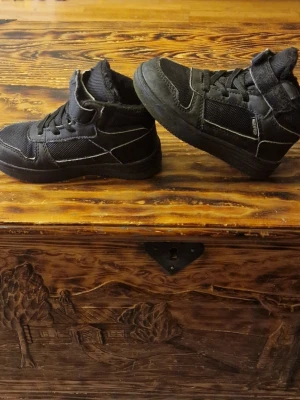 Svarta fodrade sneakers - Använda en säsong. Skav framme vid tån på höger sko. Fodret ser slitet ut men sulan är hel och de bör hålla för iaf ett barn till. Stl 26. Det var svårt att mäta innermåttet men jag får det till ca 16 cm.