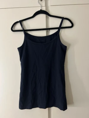 Mörkblå enkel linnetopp - Mörkblå linnetopp med smala axelband och rundad halsringning. Toppen har en rak passform och är tillverkad i ett mjukt material som känns skönt mot huden. Perfekt att styla lager på lager eller bära som den är.