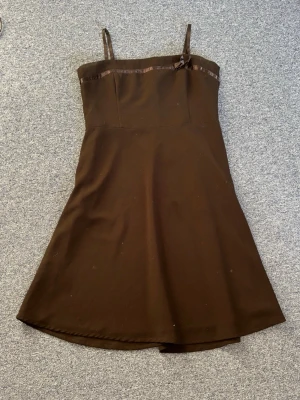 Svart kort klänning med rosett och korsettliknande byst - Söt svart kort klänning från HM. Med smala axelband och en liten rosett vid bysten som även har korsettliknande stadga. Klänningen har en enkel A-linjeform och ett diskret band upptill. Perfekt för dig som gillar minimalistisk stil. Oanvänd utan defekter, fläckarna är endast damm då den inte kommit till användning 