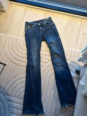 Blå bootcut jeans från True Religion - Säljer ett par mörkblå bootcut jeans från True Religion. Super fin tvätt och även slitningar där nere.