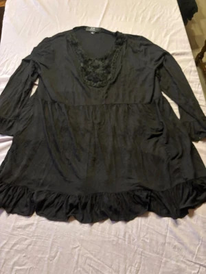 Svart blus med spetsdetaljer från ZAY - Svart blus från ZAY i storlek XL med vacker spets och broderade blommor runt den djupa ringningen. Blusen har trekvartsärm och volangkant nedtill för en extra feminin touch. Perfekt för dig som gillar romantiska detaljer.