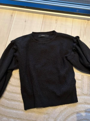 Svart stickad tröja med volanger  - Snygg svart stickad tröja från Veromoda med volanger vid ärmarna. Även lite ribbad i stickningen. 