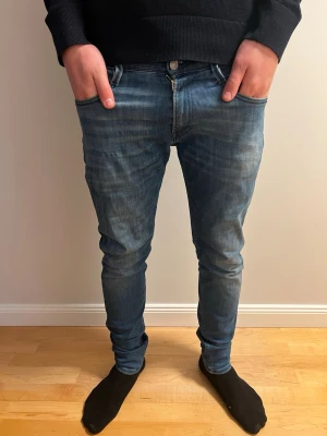 Blå skinny jeans från Replay - Säljer ett par blå skinny jeans från Replay med klassisk femficksdesign och snygga slitningar. Jeansen har en smal passform och är tillverkade i stretchigt denimtyg för extra komfort. Perfekta för en trendig och avslappnad stil.