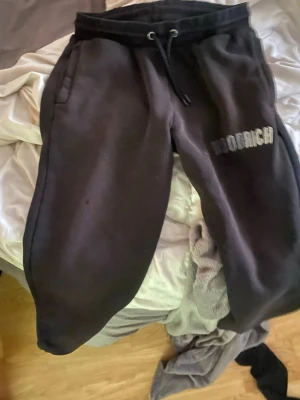 Svarta Hoodrich mjukisbyxor - Säljer ett par svarta mjukisbyxor från Hoodrich med broderad logga på ena benet. Byxorna har dragsko i midjan och sidofickor. Perfekta för chill dagar eller streetwear-stil. Materialet känns mjukt och bekvämt.