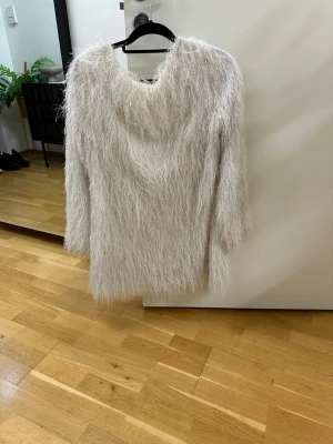 Ljusgrå fluffig stickad klänning  - Supersnygg ljusgrå stickad klänning med fluffig, långhårig struktur och djup urringning i ryggen. Klänningen har långa ärmar och en lös, avslappnad passform. Perfekt för dig som vill sticka ut med en unik och trendig look.