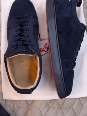 Mörkblå sneakers från Christian Louboutin - Snygga mörkblå sneakers i mocka från Christian Louboutin med klassisk låg profil och svarta snören. Skorna har en röd sula som är typisk för märket och en stilren design som passar till det mesta. Insidan är ljusbeige och materialet känns lyxigt. Det fins knappast något tecken på användning och det fins rum för att snacka om priset. Efter som dom inte använd längre pga jag har flera par och kommer inte till användning. Så skriv till mig om ni är sugna på dem 