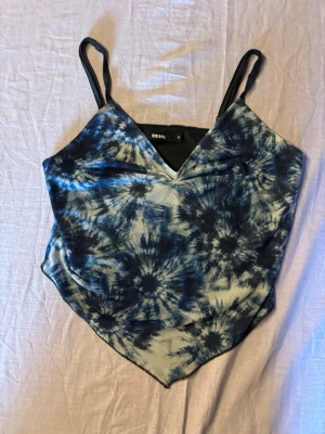 Blå batik linnetopp från Bik Bok - Trendig linnetopp från Bik Bok med blått och vitt batikmönster. Toppen har smala axelband och en spetsig nederkant som ger en cool look. Perfekt till sommaren och lätt att matcha med jeans eller kjol.