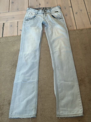 Ljusblå raka jeans i denim - Säljer ett par ljusblå jeans med rak passform och klassisk femficksdesign. Jeansen har en tvättad look och är tillverkade i mjuk denim. Perfekta för dig som gillar en avslappnad och stilren vibe.