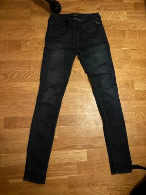 Mörkblå slim fit jeans från Replay - Säljer ett par mörkblå slim fit jeans från Replay med klassisk femficksdesign och snygga slitningar. Jeansen har en smal passform och är tillverkade i stretchigt denimtyg för extra komfort. Perfekta för dig som gillar en stilren och modern look.