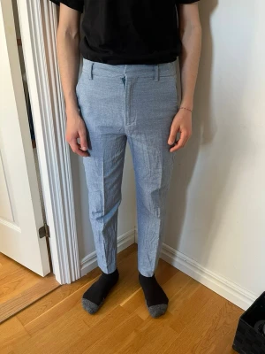 Ljusblå kostymbyxor  - Säljer ett par ljusblå kostymbyxor med smal passform och pressveck. Byxorna har bälteshällor, dragkedjegylf och är tillverkade i ett tunt, vävt material som känns luftigt. Perfekta för en stilren look.