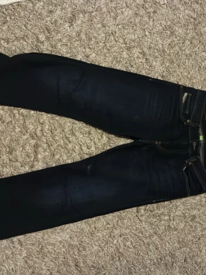 Nya Mörkblå jeans från Diesel w29 L30 - Säljer ett par mörkblå jeans från Nudie Jeans med klassisk femficksdesign och raka ben. Jeansen har kontrastsömmar och en snygg läderpatch bak i midjan. Perfekta för dig som gillar stilrena och tidlösa jeans.