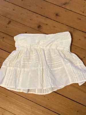 Vit kortkjol med broderade detaljer - Söt vit kortkjol med broderade detaljer och lätt volang. Kjolen har bred resår i midjan och är gjord i ett tunt, luftigt bomullstyg. Perfekt för varma dagar och enkel att matcha med olika toppar. Kan ha som kjol och topp men är inte stretchig så kolla måtten nogrannt!