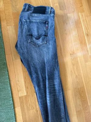 Grå replay grover  - Säljer ett par grå jeans från replay med slitningar. Klassisk femficksmodell med svarta sömmar på bakfickan och en avslappnad passform. Perfekta för en cool och avslappnad stil sitter ungefär som Levis 501 jag är 185 cm lång och dom passar bra i längd.