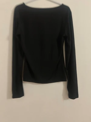 Svart långärmad tröja  - En enkel svart långärmad tröja med rund halsringning. Toppen har en klassisk och stilren design som passar till det mesta. Materialet känns mjukt och stretchigt, vilket gör den bekväm att bära.