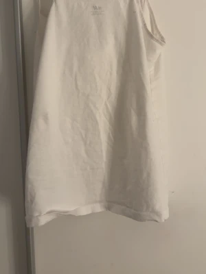 Vit ärmlös linnetopp från H&M - En enkel vit linnetopp från H&M med klassisk rak passform och ärmlös design. Perfekt till sommaren och lätt att matcha med olika stilar. Har dock 3 blåa fläckar men man märker det knappt 
