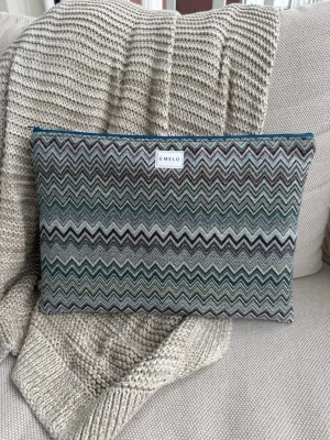 Mönstrad datorväska från Emelo - Snygg datorväska från Emelo med zigzag-mönster i grönt, grått, svart och beige. Väskan har en mjuk textil utsida och stängs med dragkedja i blått. Perfekt för att skydda din laptop med stil och unik design. Passar laptop med maxmått: 33x24cm