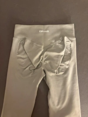 Grå scrunch leggings från DFYNE - Säljer ett par ljusgrå scrunch leggings från DFYNE med hög midja och ribbad linning. Materialet är stretchigt och följsamt, perfekt för gymmet eller träning. Snygg passform som framhäver formerna och sitter bekvämt hela dagen.